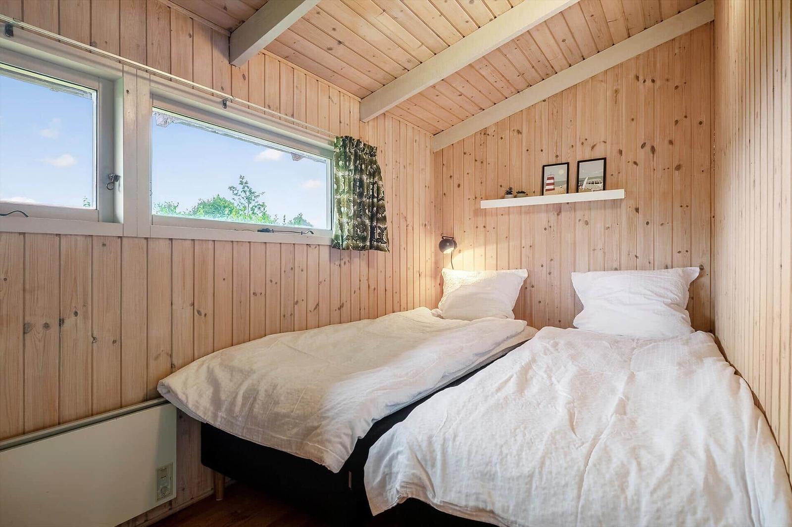 Zwei Einzelbetten in einem Holzhauszimmer mit Fenster und Wandregal.