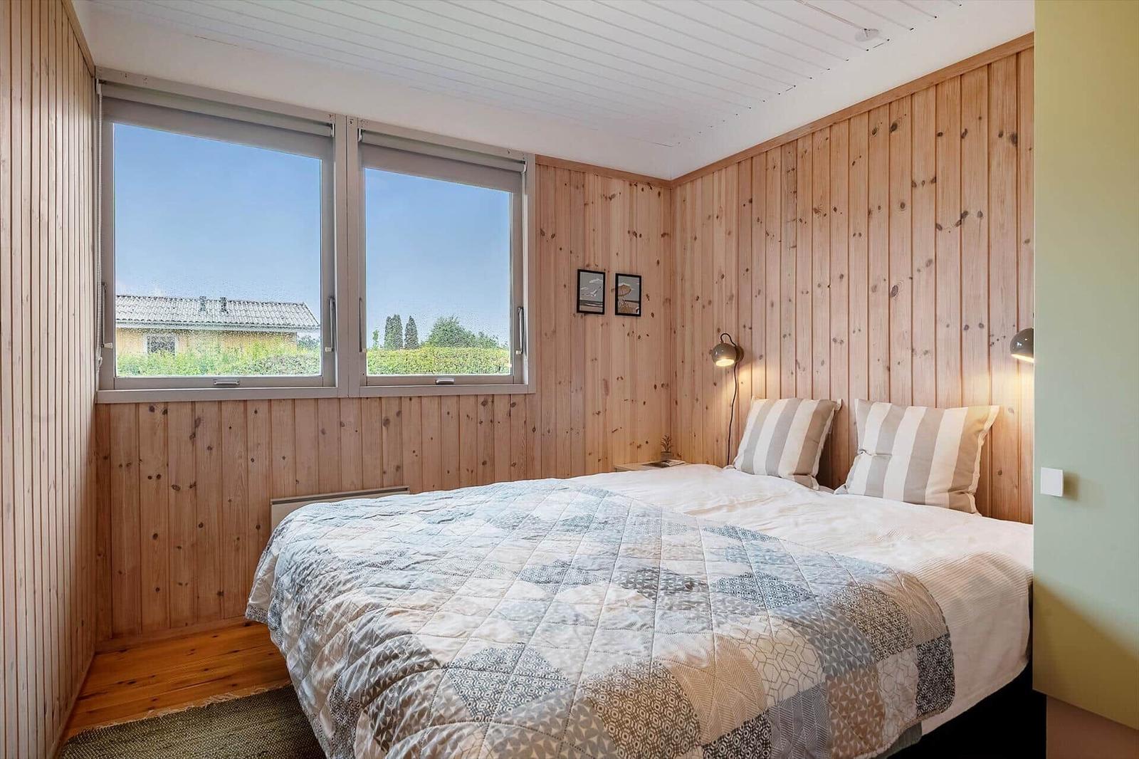 Schlafzimmer mit Holzwand und großem Fenster mit Blick auf die Landschaft.