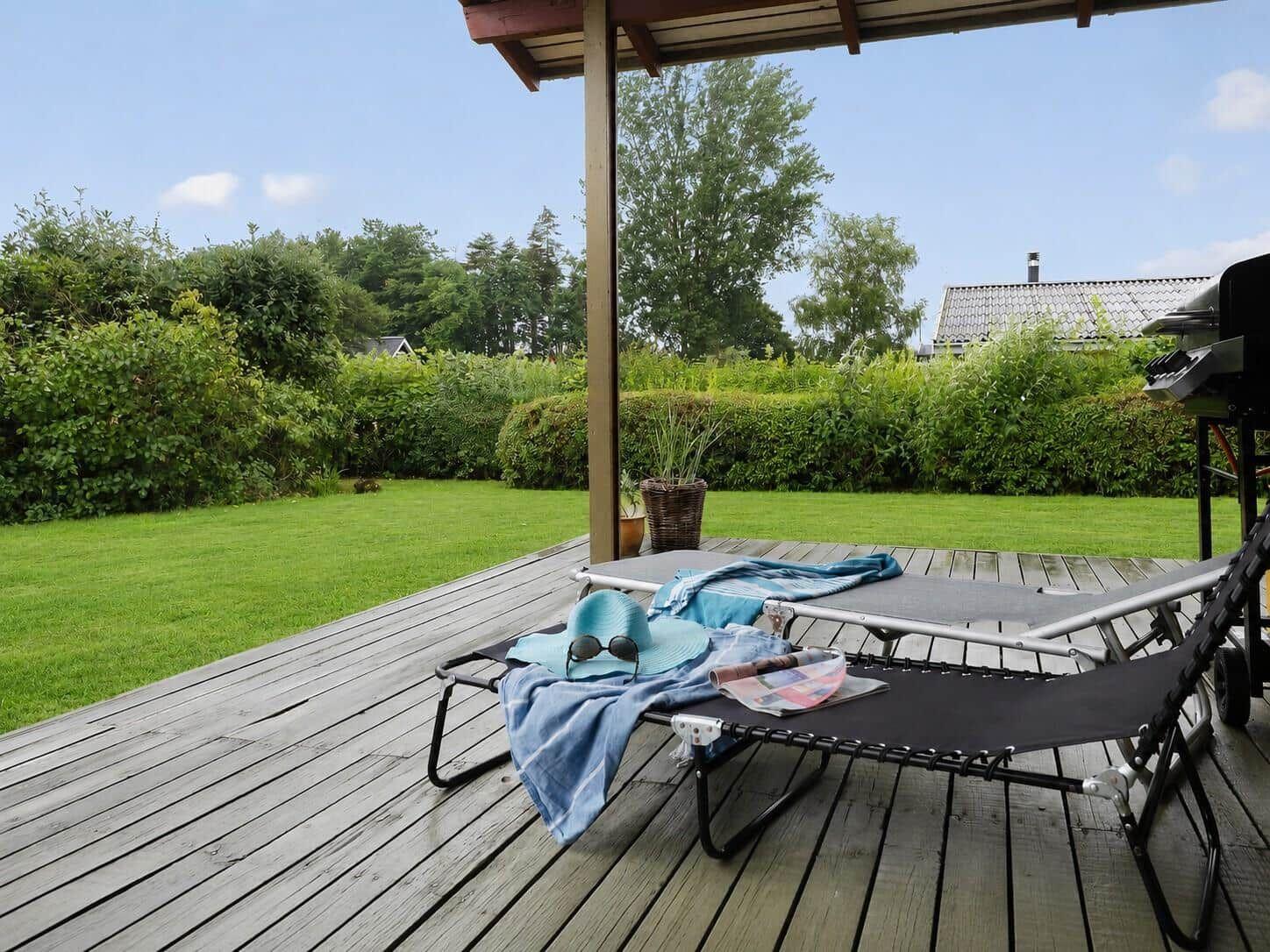 Terrasse mit Liegestühlen, Grill und Blick auf grünen Garten.