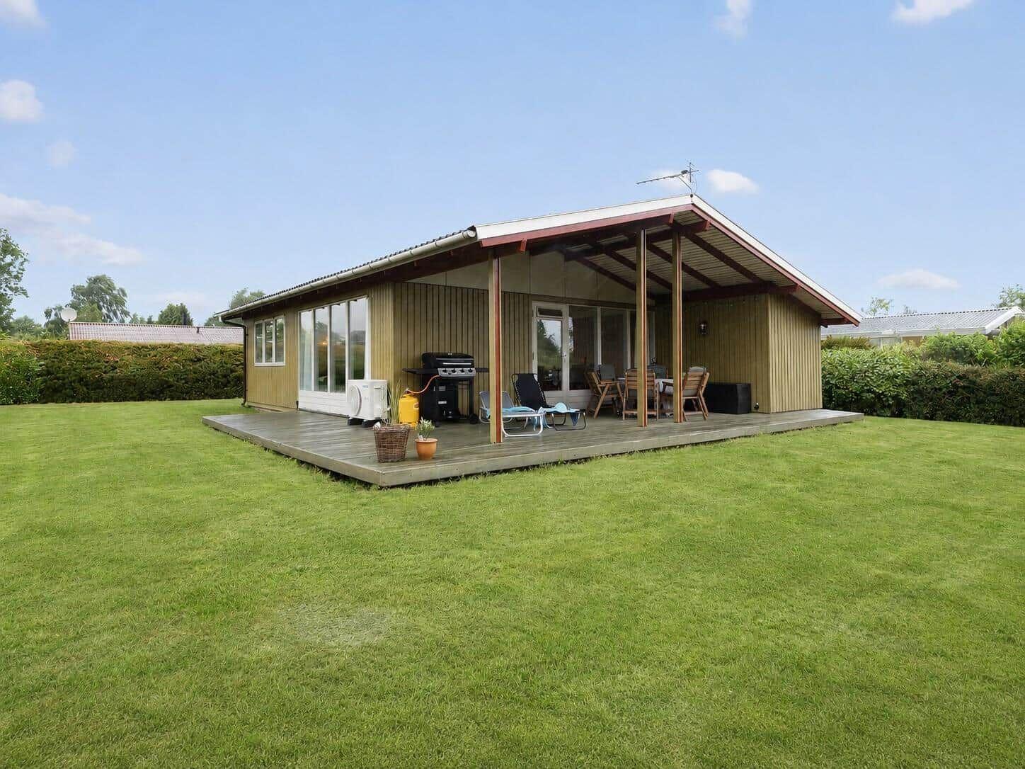 Moderne Ferienhaus mit Terrasse, Grill und Garten. Sicht auf grünen Rasen und Hecken.