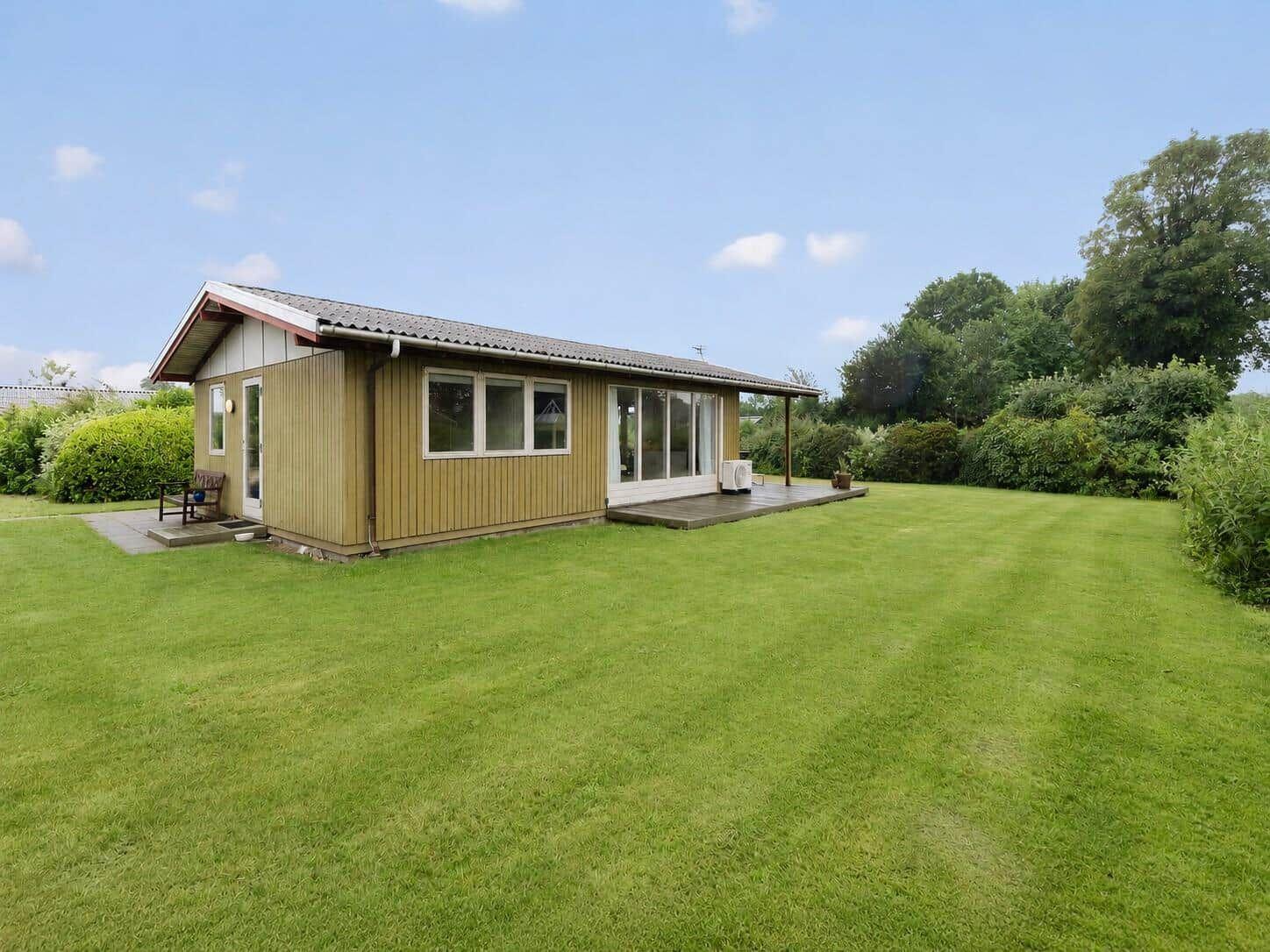 Ein kleines Haus mit Holzfassade und Terrasse auf einer grünen Wiese.