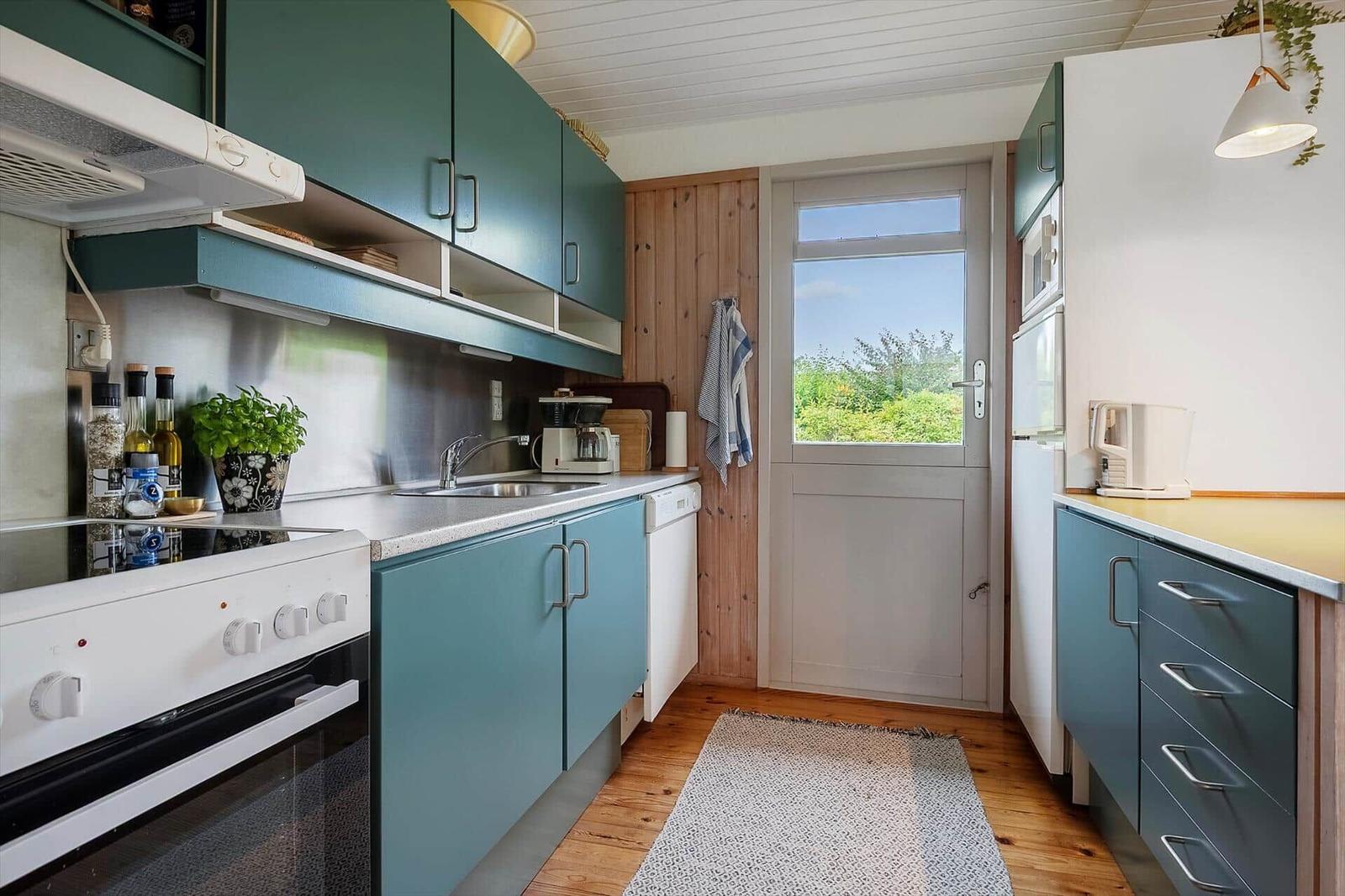 Küche mit blauen Schränken, Edelstahlspüle und Holzboden. Tür führt nach draußen.