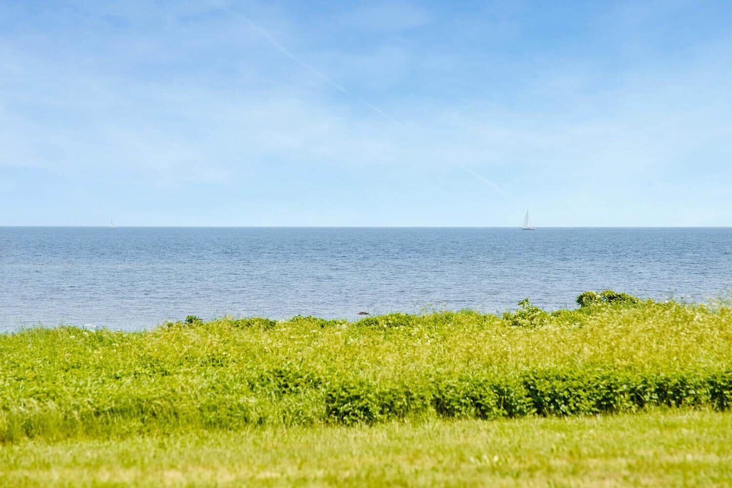 Grünes Feld mit Blick auf das Meer und zwei Segelboote im Hintergrund.