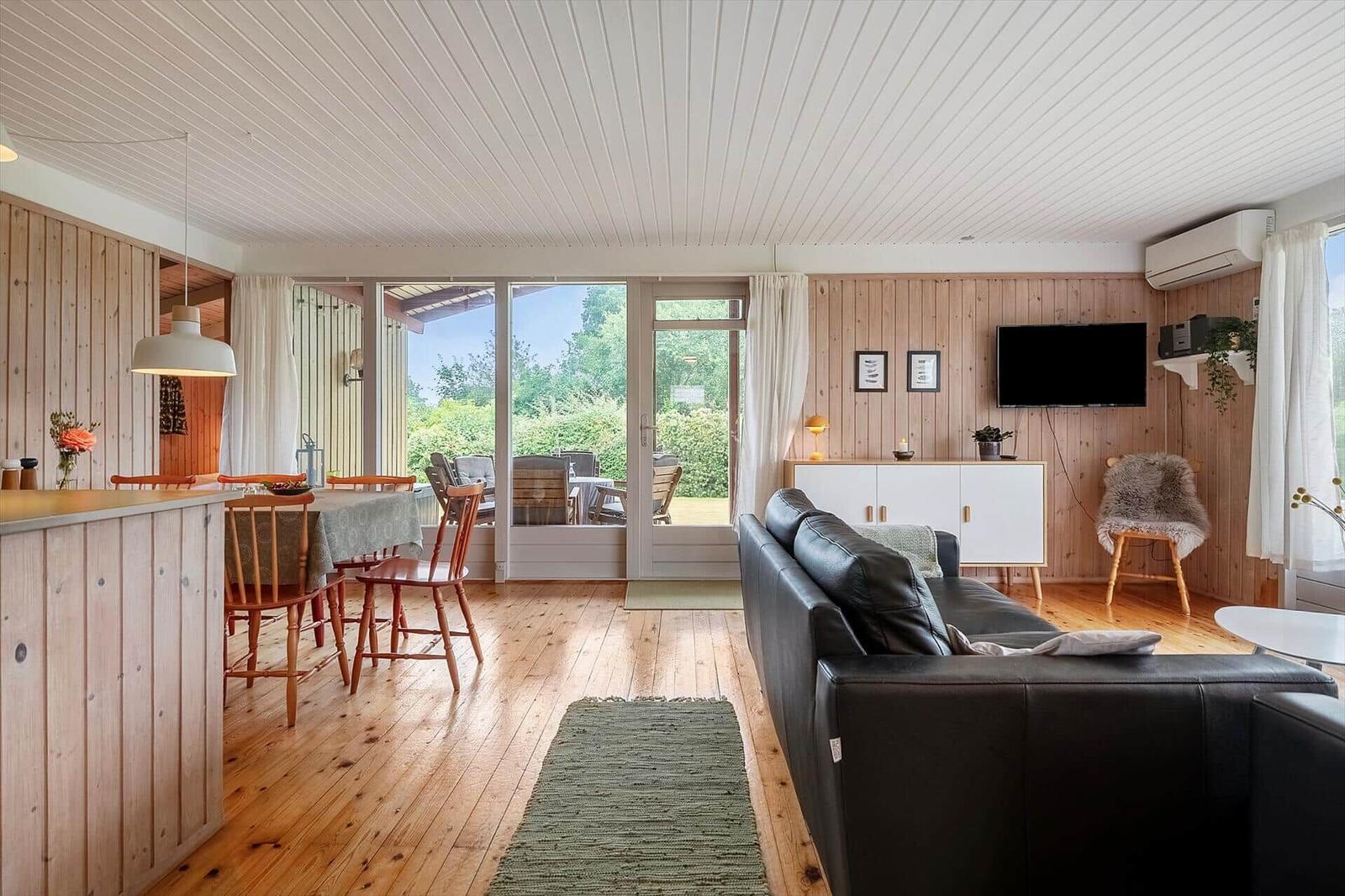 Wohn- und Essbereich mit Holzdecke, Sofa und Blick auf den Garten.