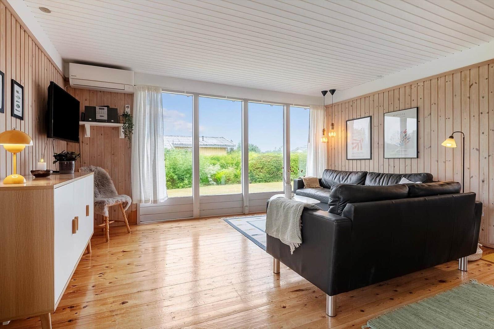 Wohnzimmer mit Holzwänden, großem Fenster und schwarzem Sofa.