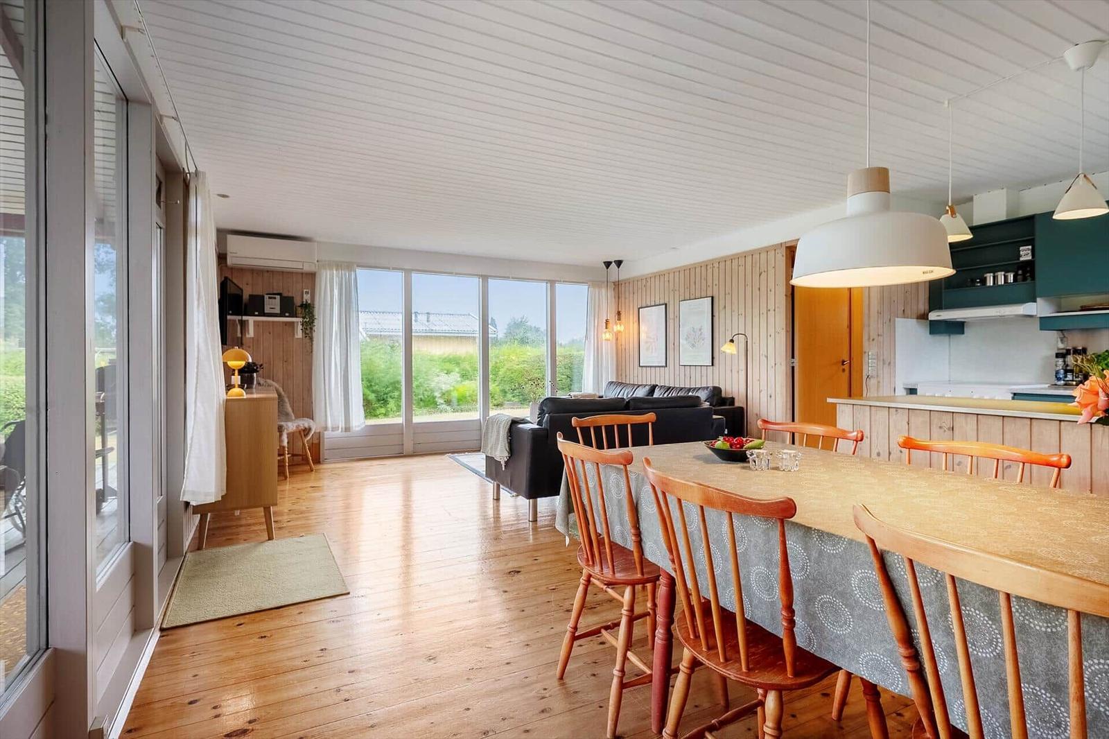 Ein Essbereich mit Holztisch und Stühlen. Im Hintergrund Küche und Wohnzimmer mit großem Fenster.