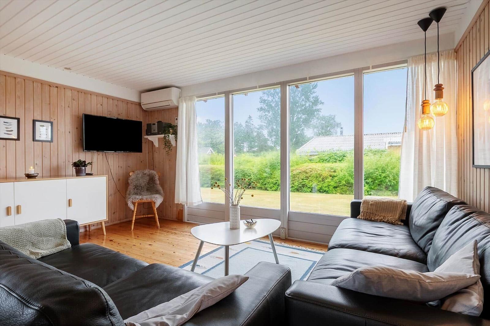 Wohnzimmer mit großem Fenster, Ledersofa und Holzwand