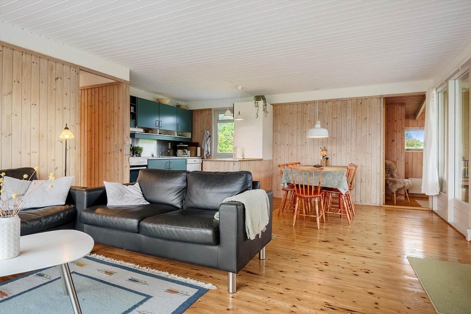 Wohn- und Essbereich mit Holzwand, Sofa, Tisch und Stühlen.