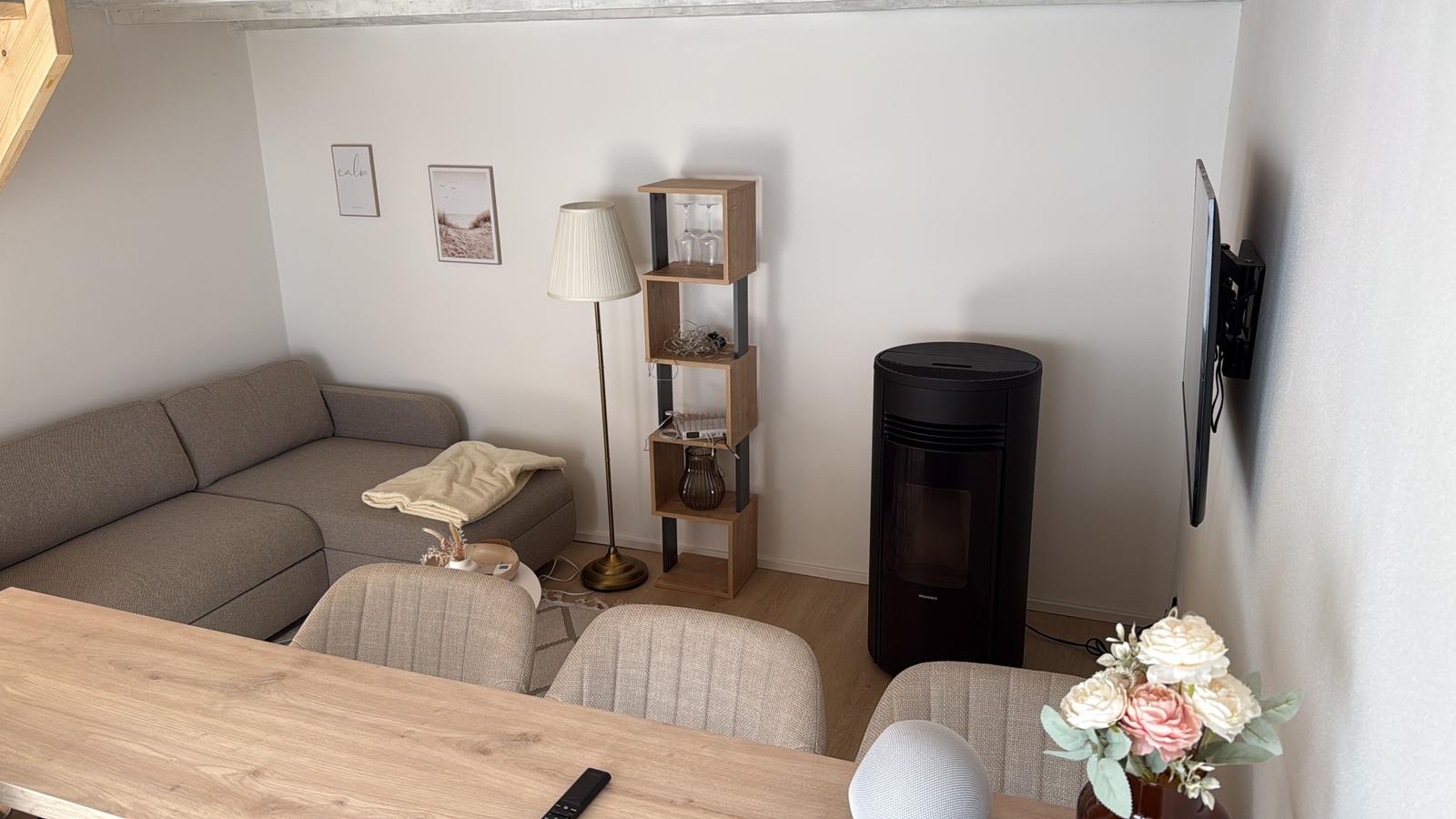 Wohnzimmer mit Sofa, TV und Stehlampe. Holztisch mit Stühlen und Blumen.