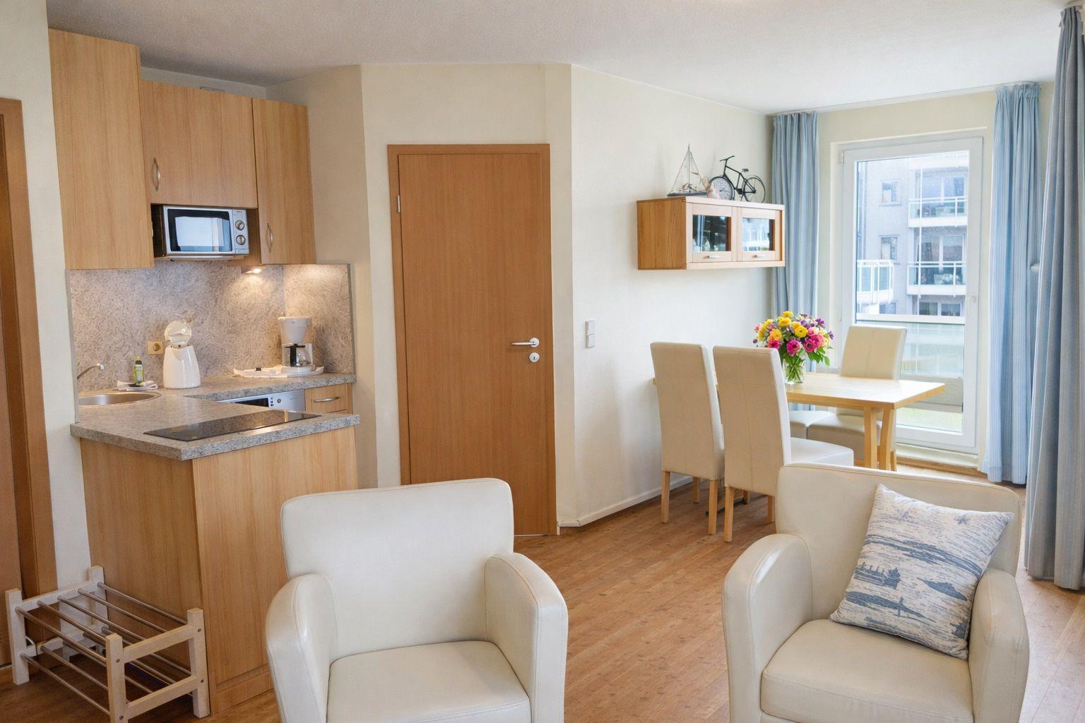 Wohnbereich mit Küchenzeile, Essplatz und zwei Sesseln. Durchgang zur Wohnung.