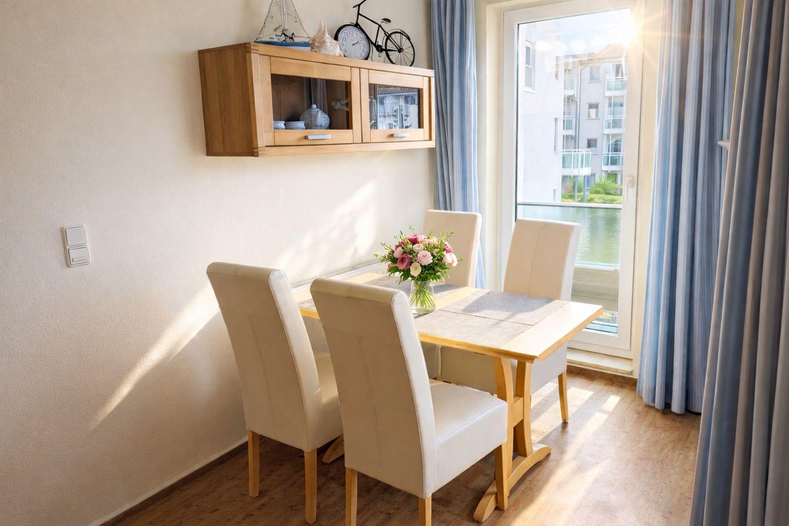 Essbereich mit Tisch, vier Stühlen und Fensterblick auf Wasser.