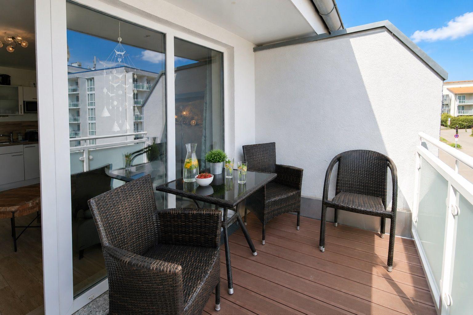 Terrace with table and three chairs, wooden floor and glass railing.
