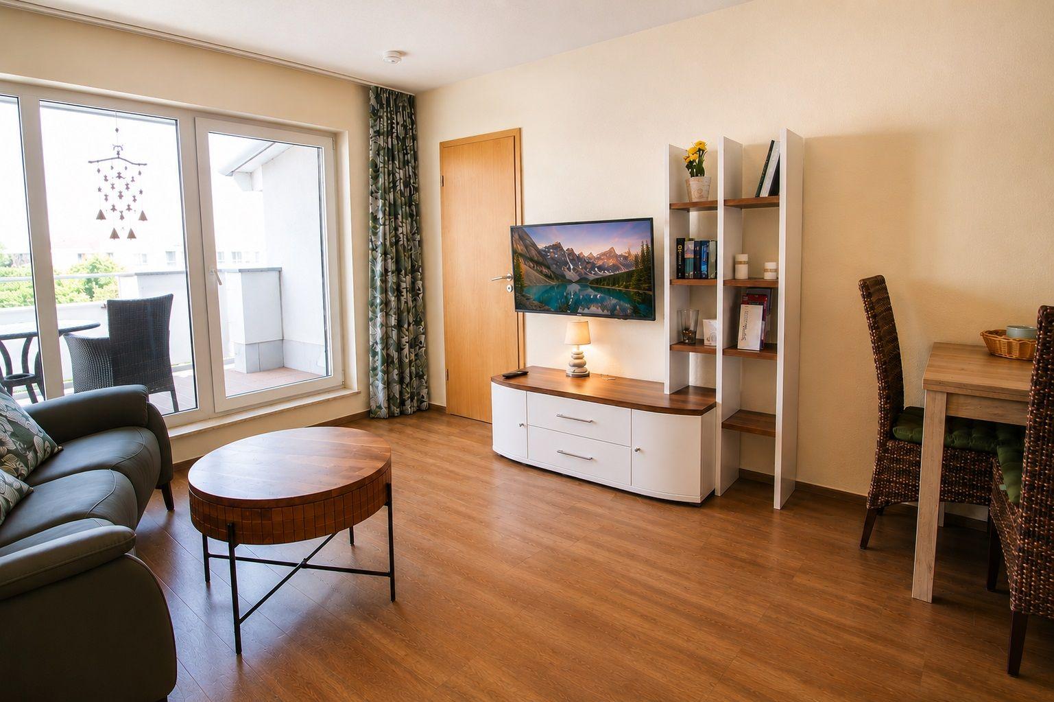 Living room with sofa, round table, TV, and dining area. Balcony with seating.