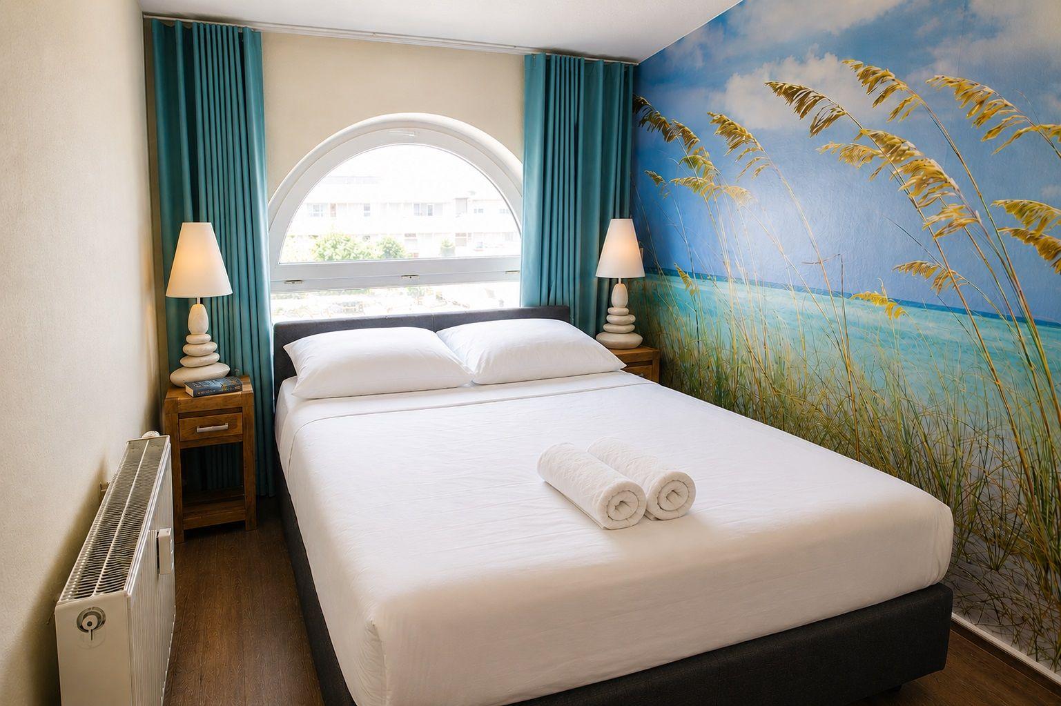 Bedroom with bed, window, and wall mural of beach scene.