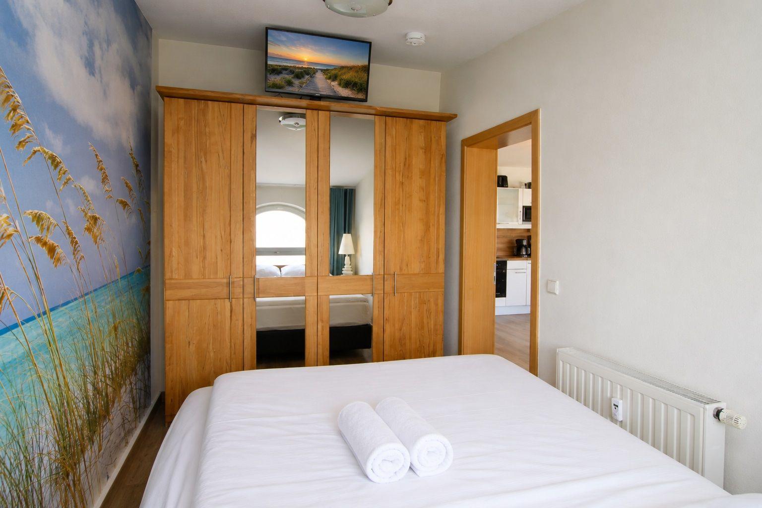 Bedroom with bed, wardrobe, and TV. Wall mural shows beach.
