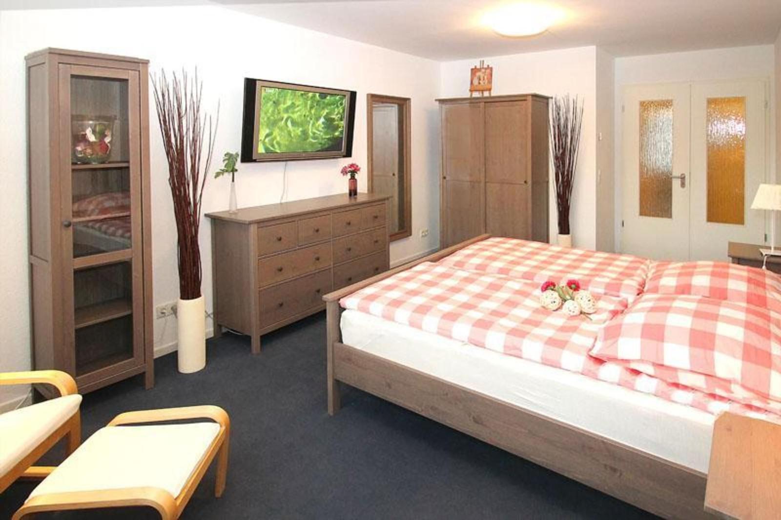 Schlafzimmer mit Bett, Kleiderschrank und Fernseher an der Wand.