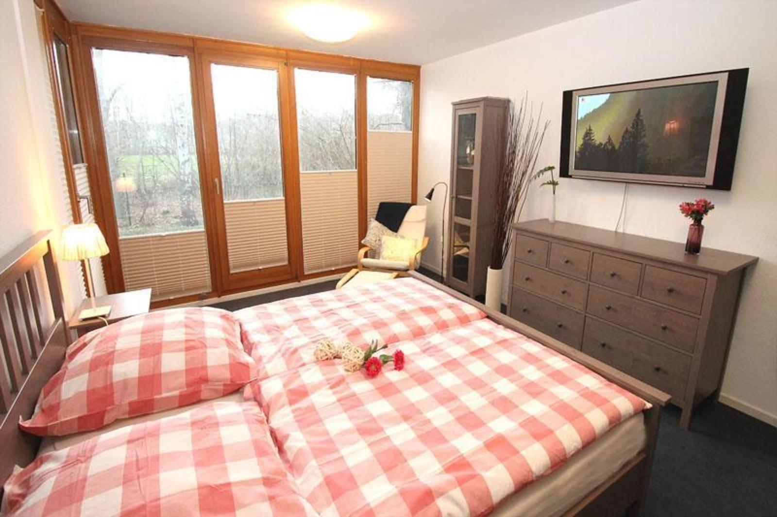 Schlafzimmer mit Doppelbett, TV und großem Fenster zur Aussicht.
