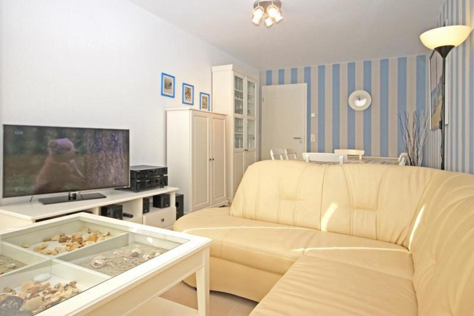 Wohnzimmer mit cremefarbenem Sofa, Glas-Tisch mit Muscheln und Fernseher