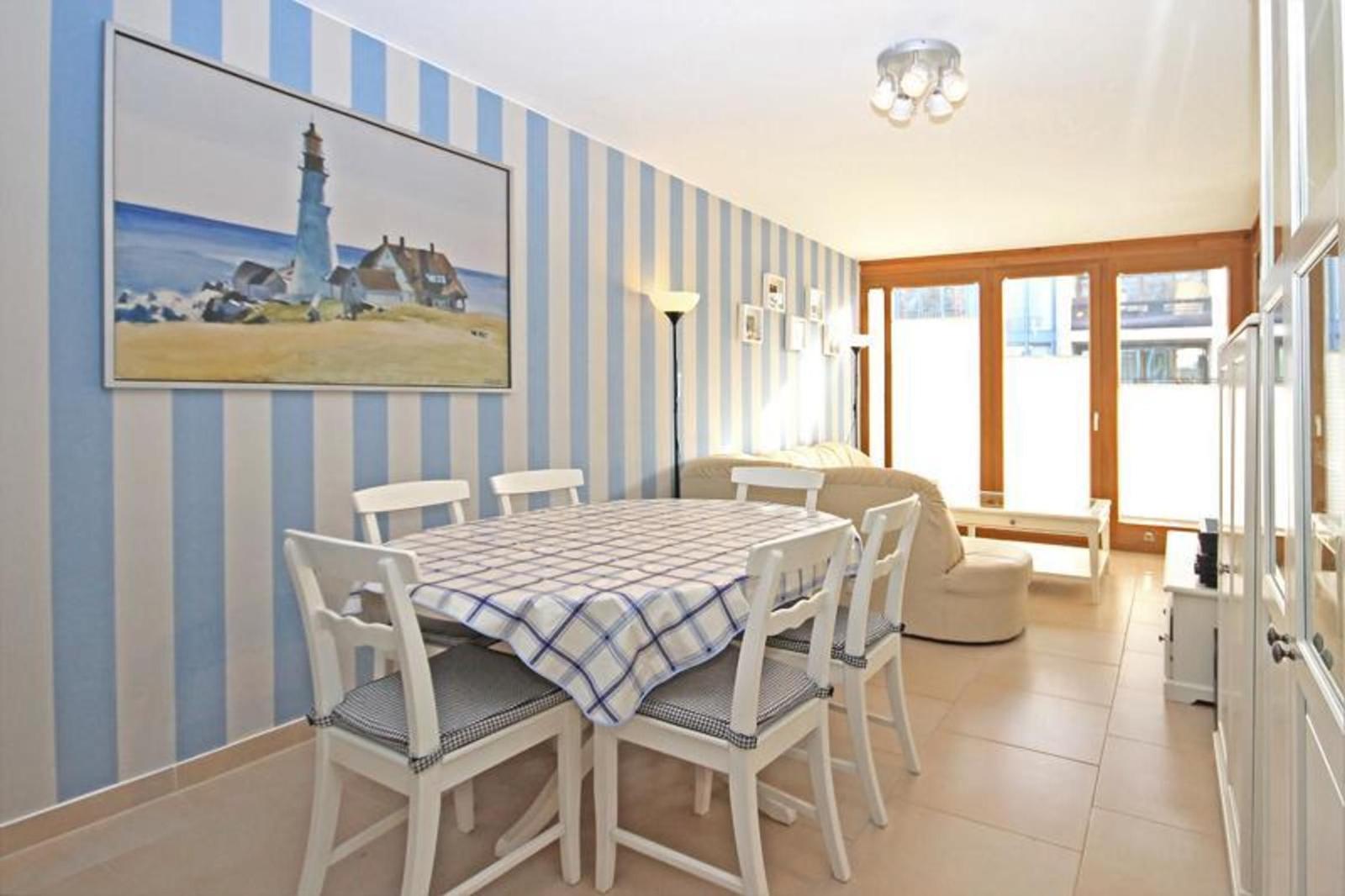 Esszimmer mit Tisch, Stühlen und Streifenwand. Durchgang zum Wohnbereich mit Fenster.