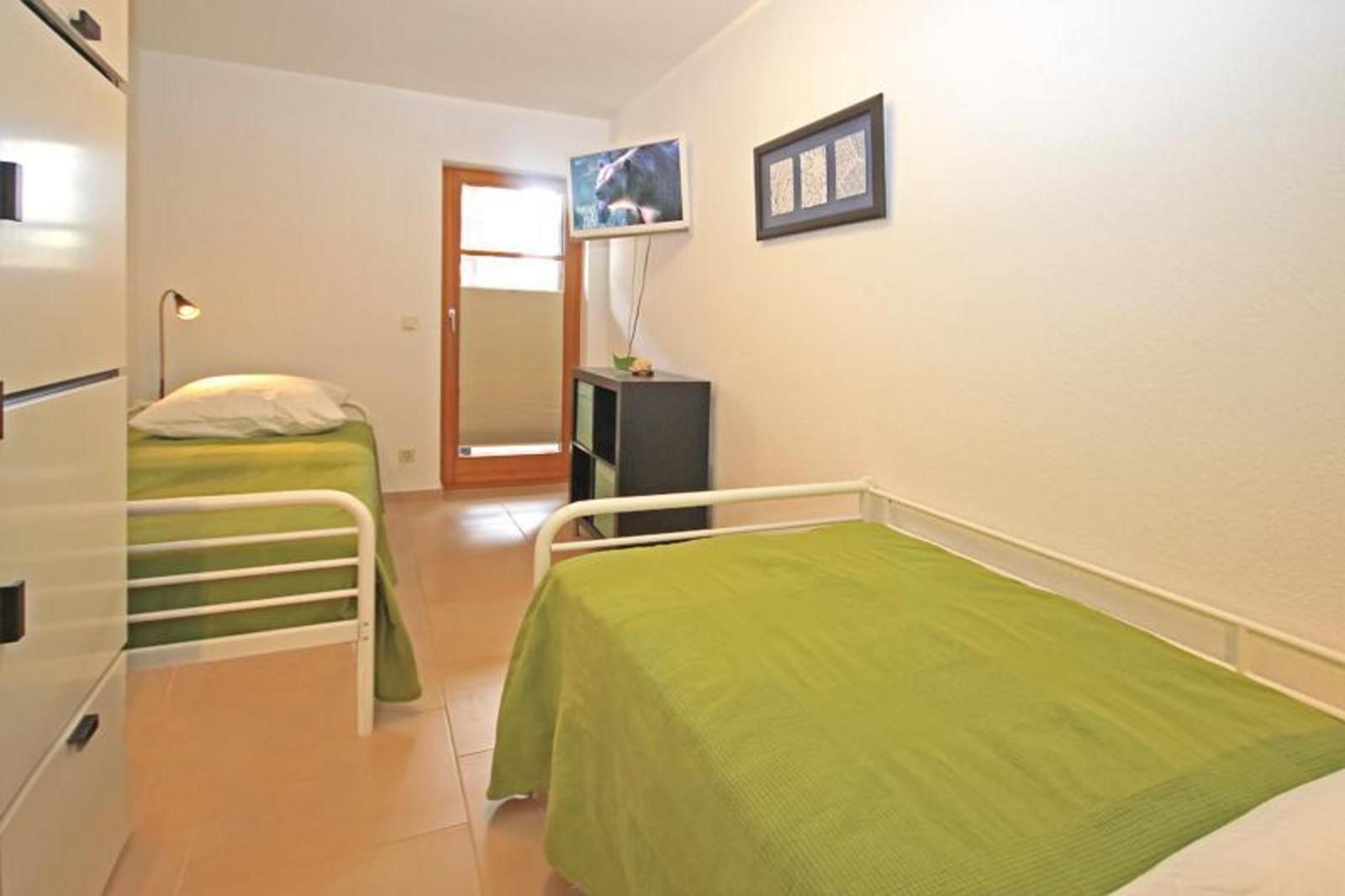 Zwei Einzelbetten mit grünen Bettwäschen, ein Schrank und ein Fernseher an der Wand.