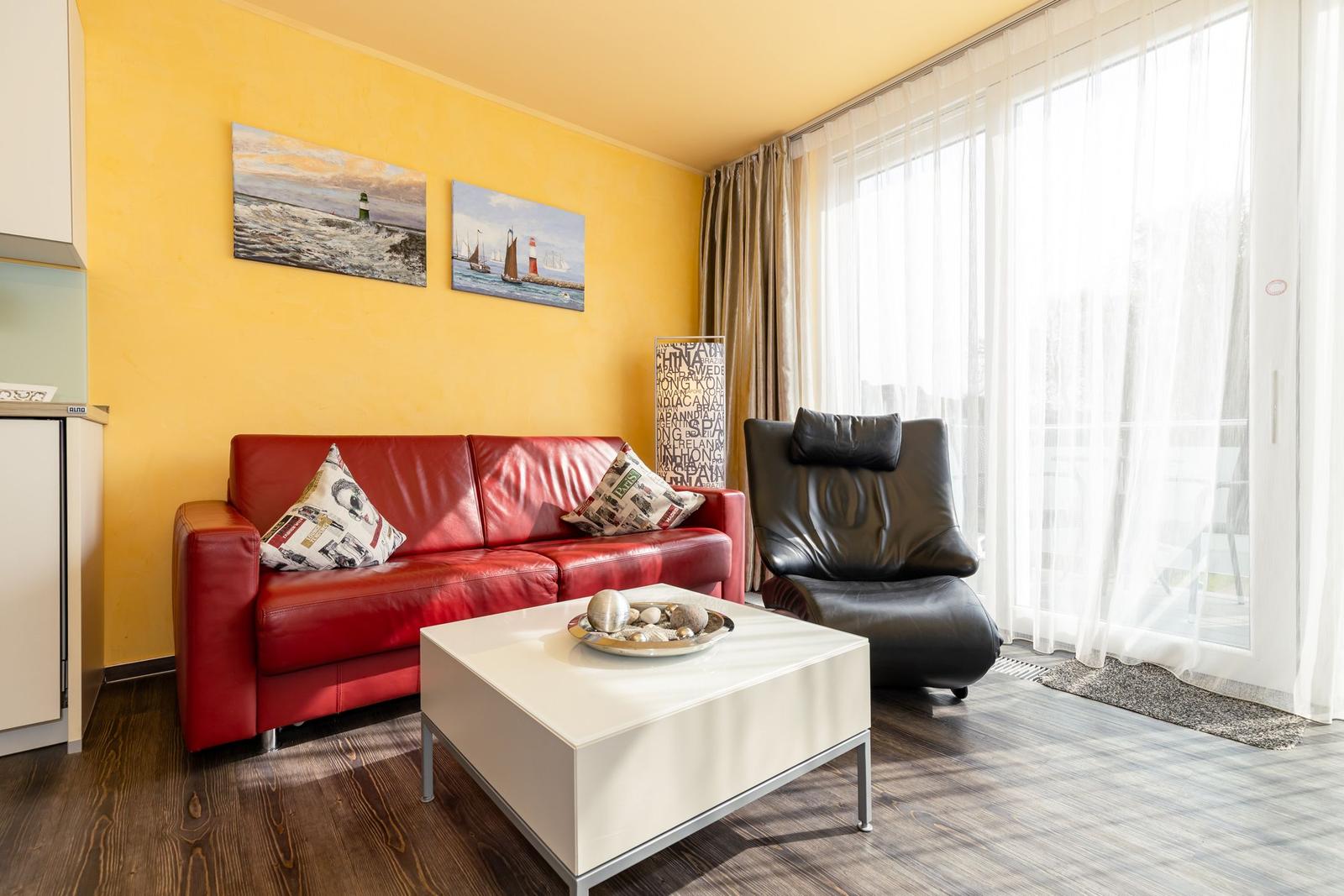 Ein Wohnzimmer mit rotem Sofa, schwarzer Ledercouch und weißem Couchtisch. Gelbe Wände und große Fenster.