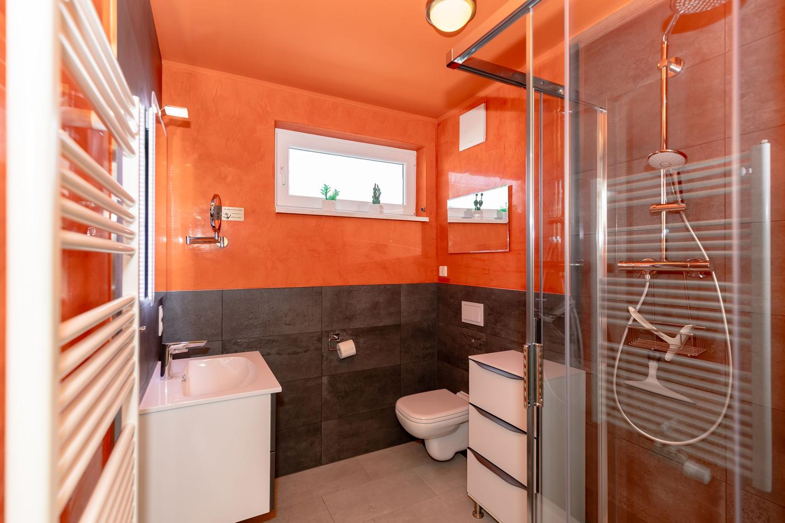 Badezimmer mit Dusche, Toilette und Waschbecken. Wände in Orange und Grau.