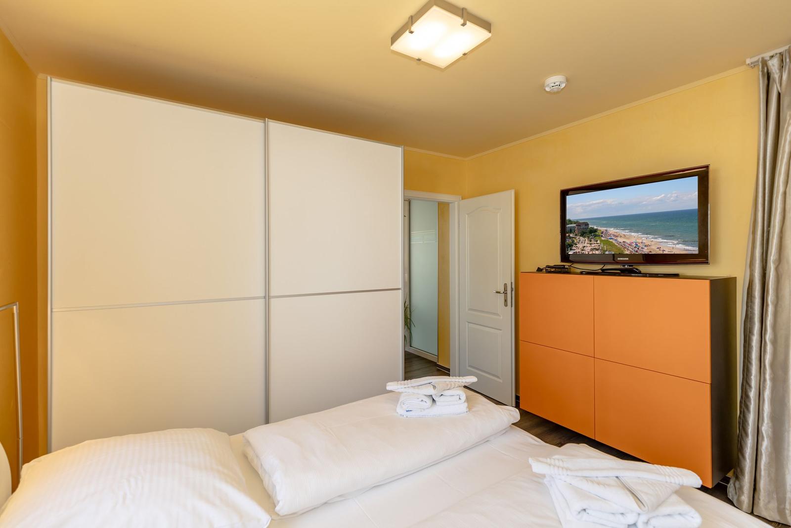 Schlafzimmer mit Bett, Schrank und Fernseher an der Wand.