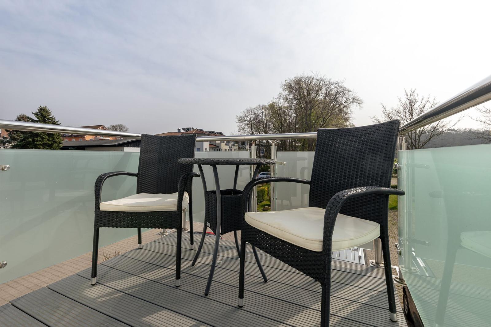Terrasse mit zwei Stühlen und Tisch, Glasgeländer und Blick auf Wohngebiet.