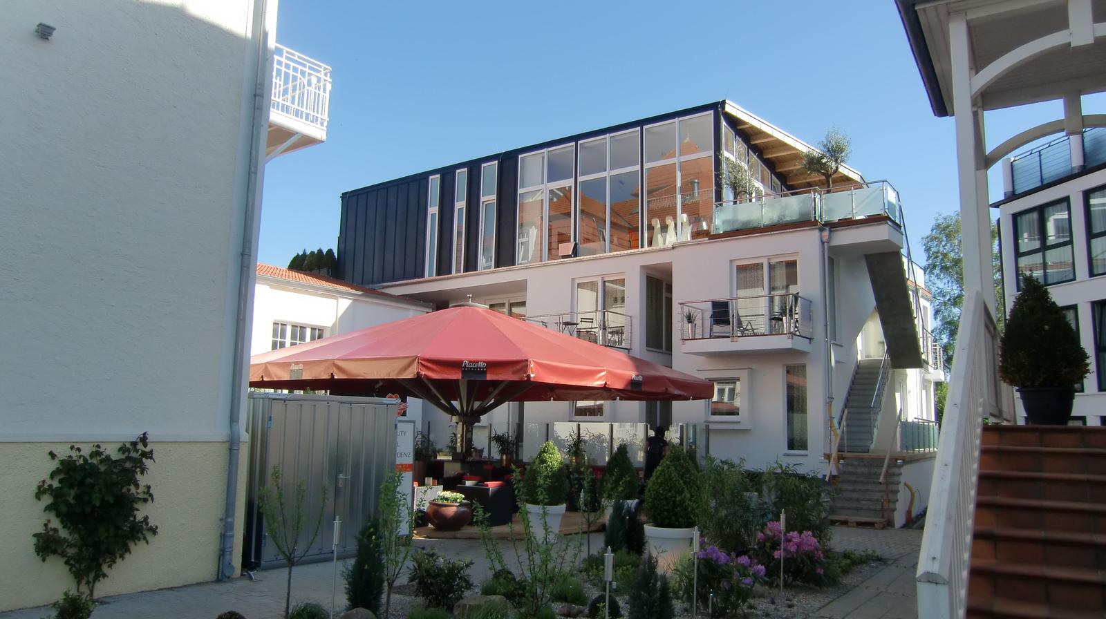 Moderne Wohnanlage mit Terrasse und Gartenbereich unter rotem Sonnenschirm.