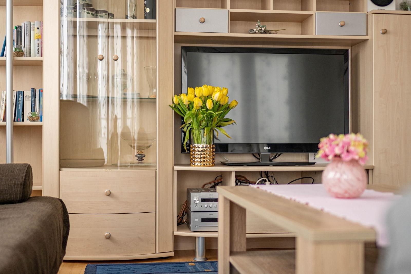 Ein Wohnzimmer mit Fernseher, Blumen und Holzmöbeln.