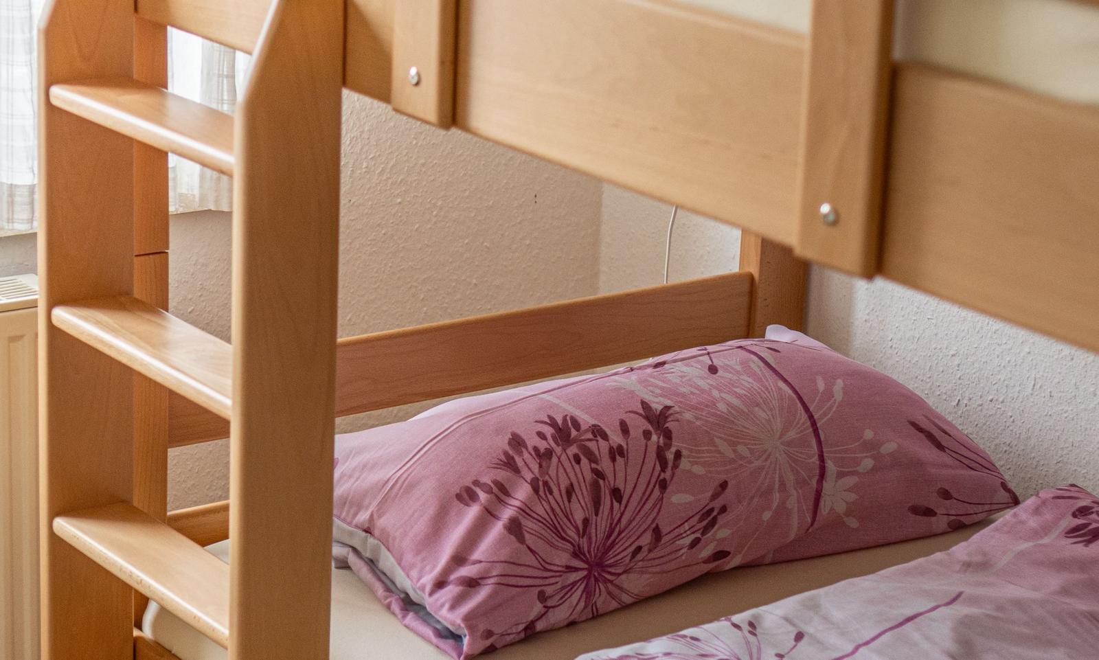 Ein Etagenbett mit Holzgestell und rosa Bettwäsche mit Blumenmuster.