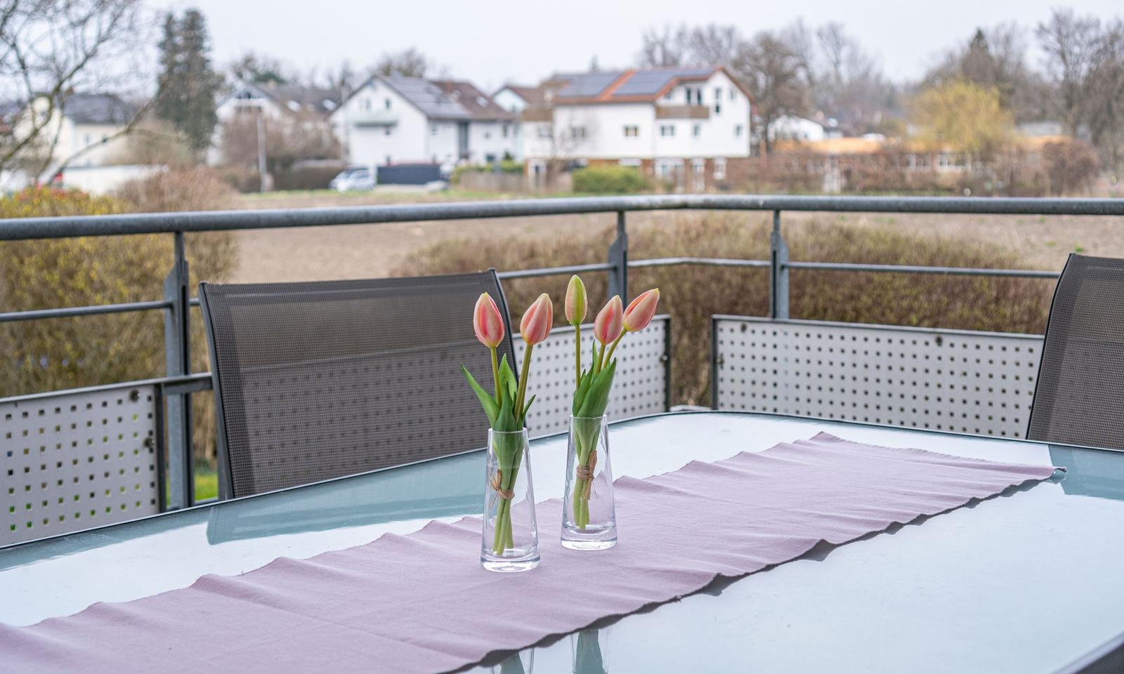 Terrasse mit Tisch, Stühlen und Tulpenblumen. Blick auf Wohnhäuser und Grünflächen.