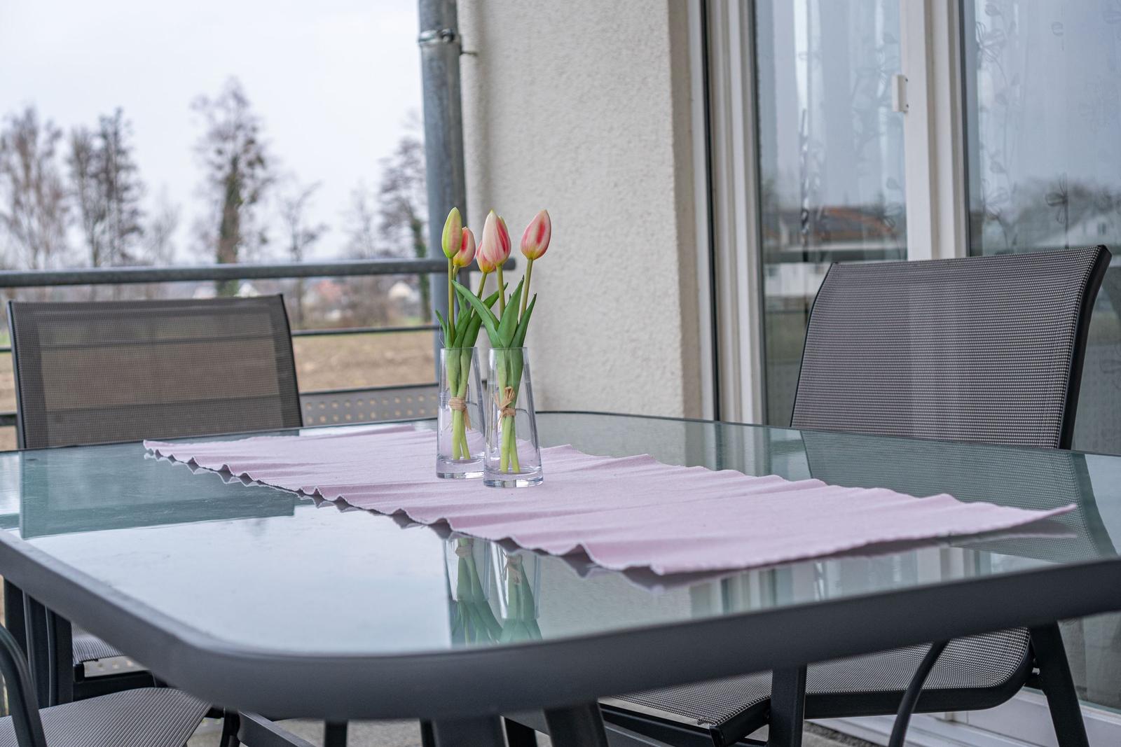 Glas-Tisch mit rosa Tischdecke und Tulpen in Vasen auf Balkon
