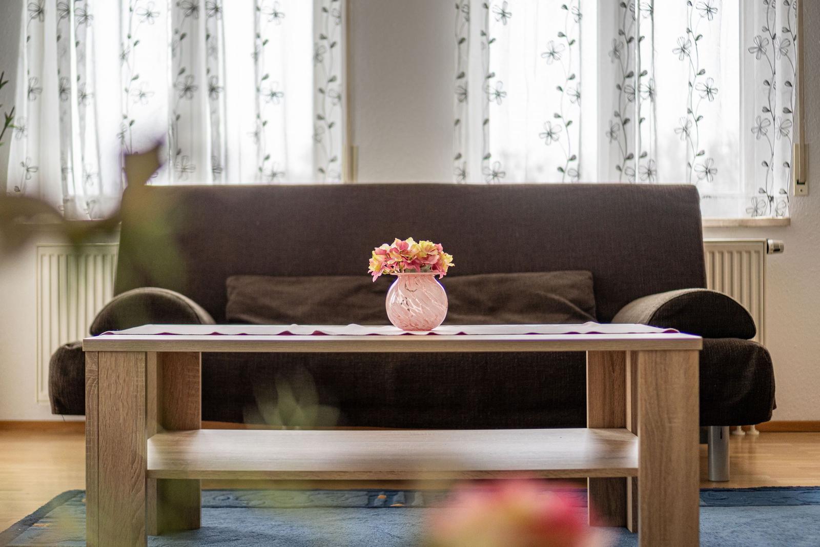 Ein Wohnzimmer mit braunem Sofa, Holztisch und Blumen in einem Vasen.
