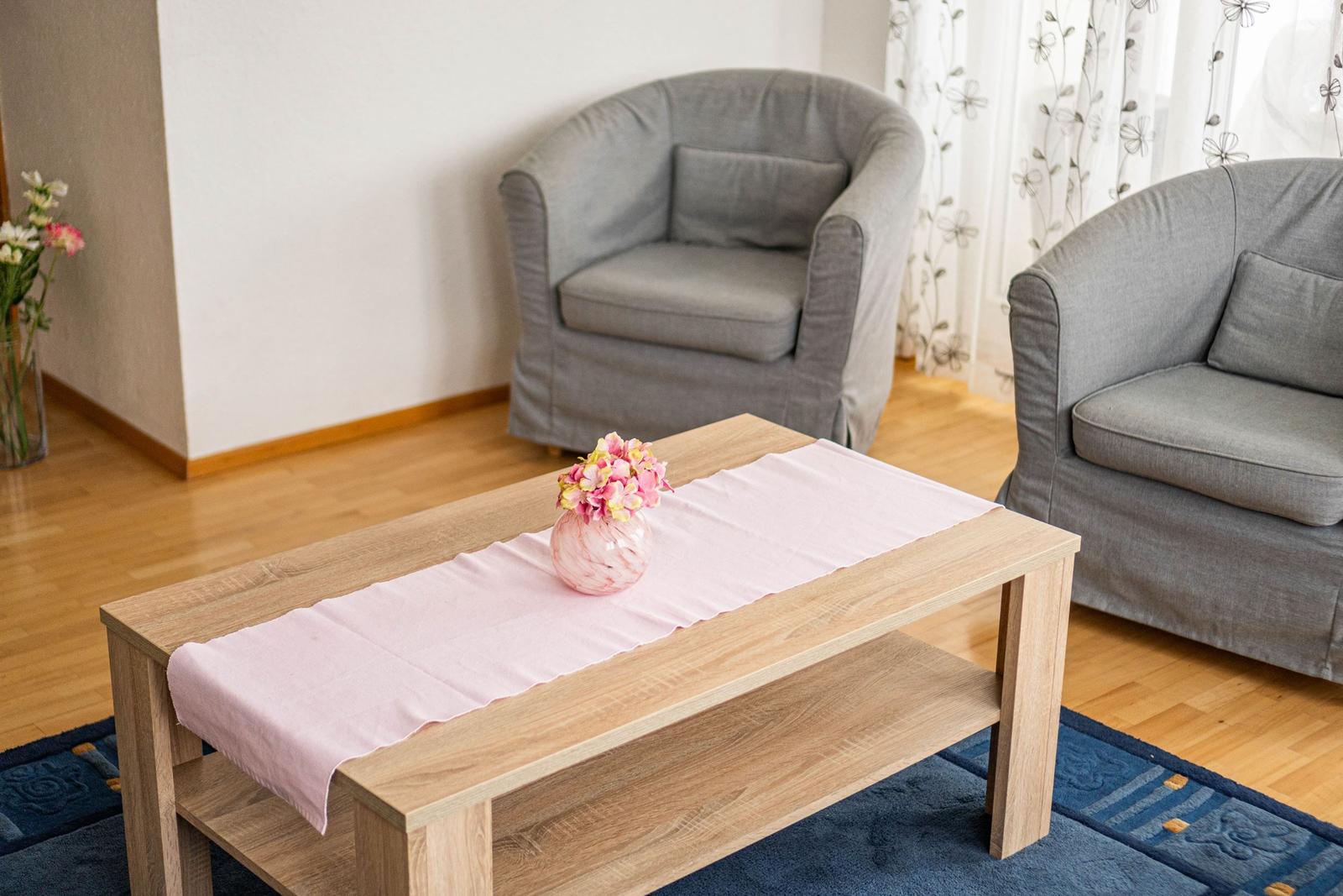 Ein Wohnbereich mit zwei grauen Sesseln, einem Holztisch und einem Blumenarrangement.