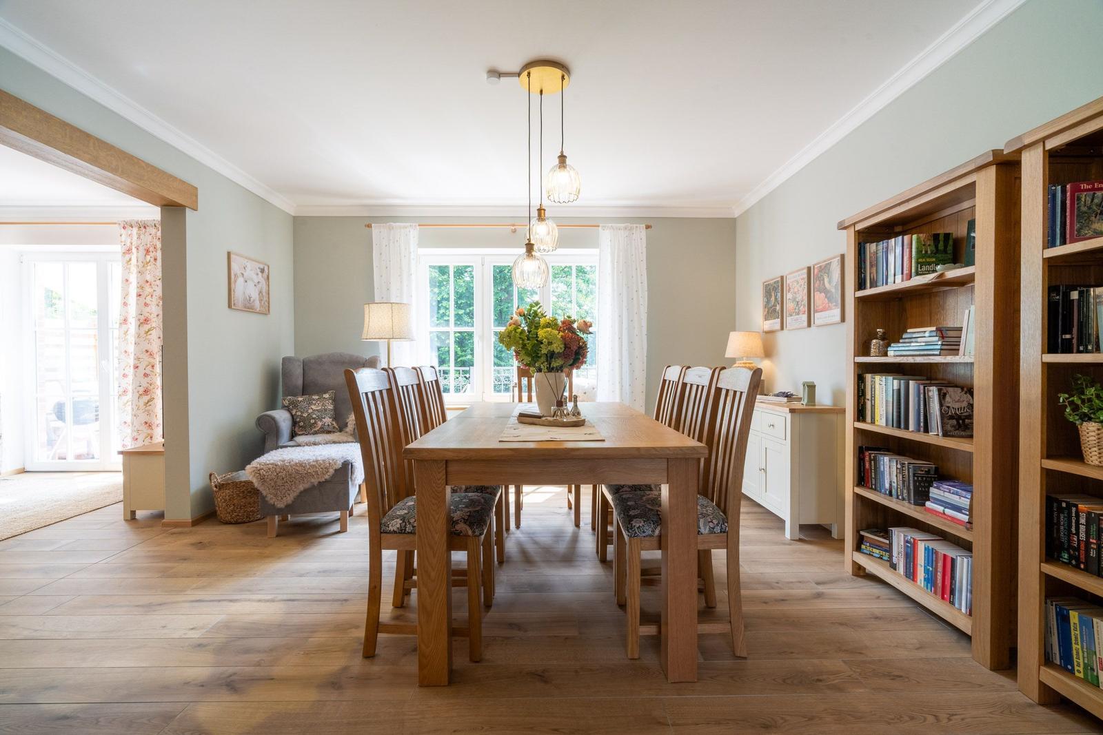 Esszimmer mit Holztisch, Stühlen und Bücherregal. Fenster mit Blick ins Freie.