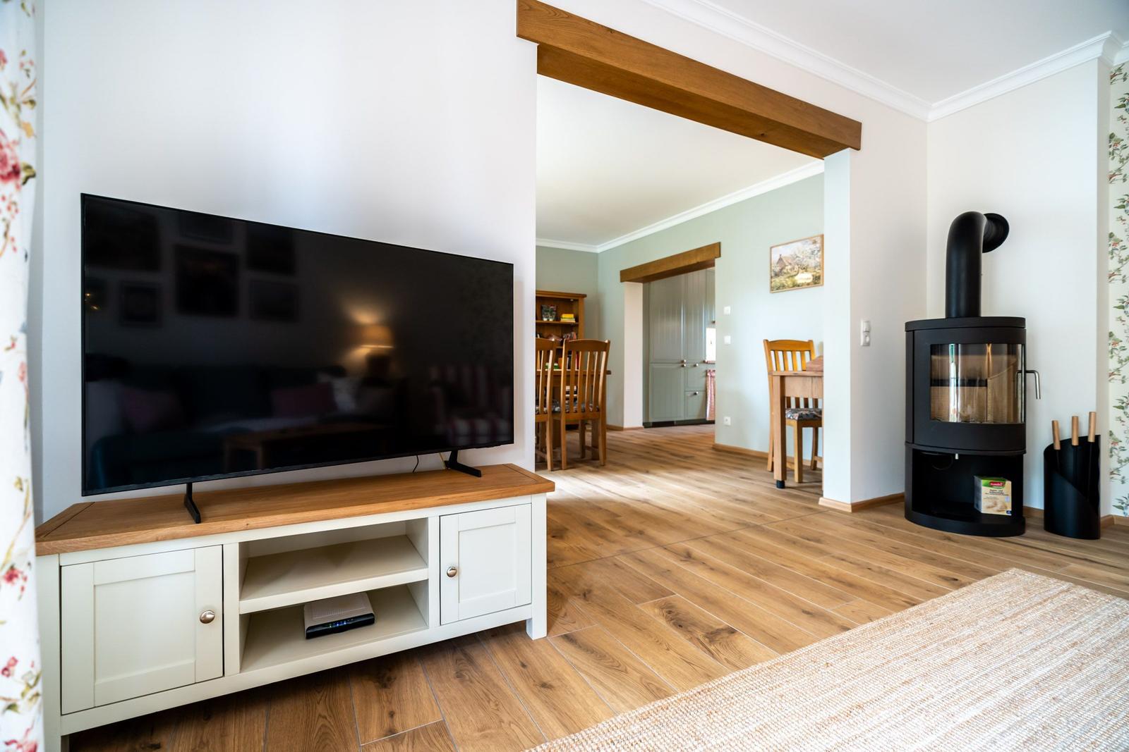 Wohnzimmer mit Fernseher, Holzofen und angrenzendem Essbereich.