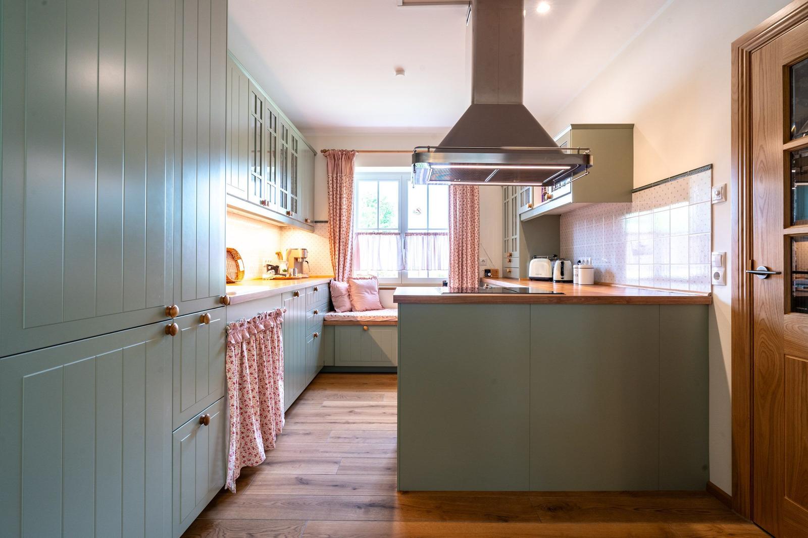 Küche mit grünen Schränken, Holzboden und Fensterbank mit Kissen.