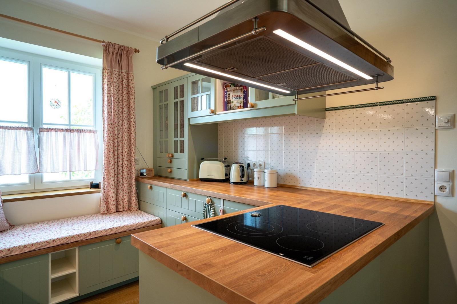 Küche mit Holzplatten, grünen Schränken und Fensterbank mit Stoffbezug.