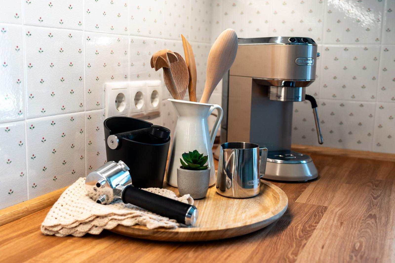 Küchenbereich mit Espressomaschine, Holzbrett und Küchenutensilien auf Holzoberfläche.