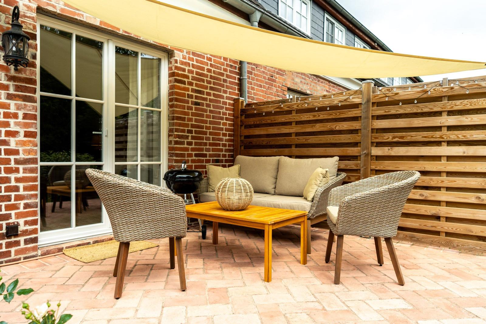 Terrasse mit Sitzgruppe, Grill und Sonnensegel. Holzgeländer und Ziegelwand.