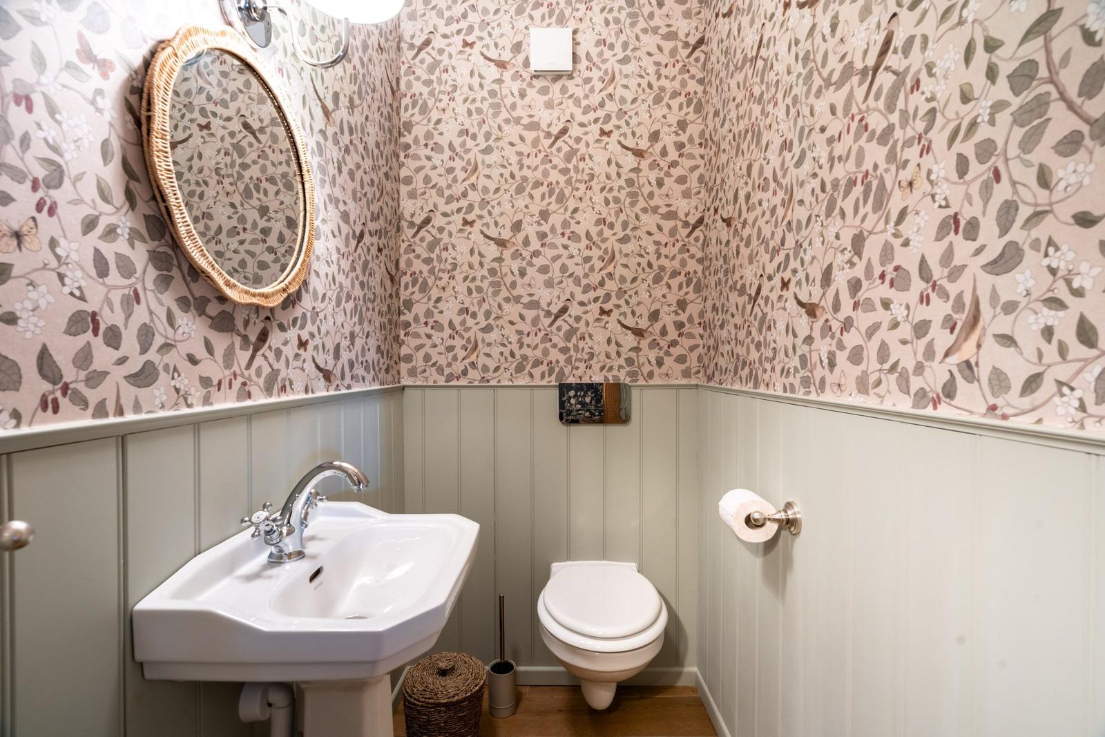 Badezimmer mit Waschbecken, Toilette und Spiegel mit Korbrahmen.
