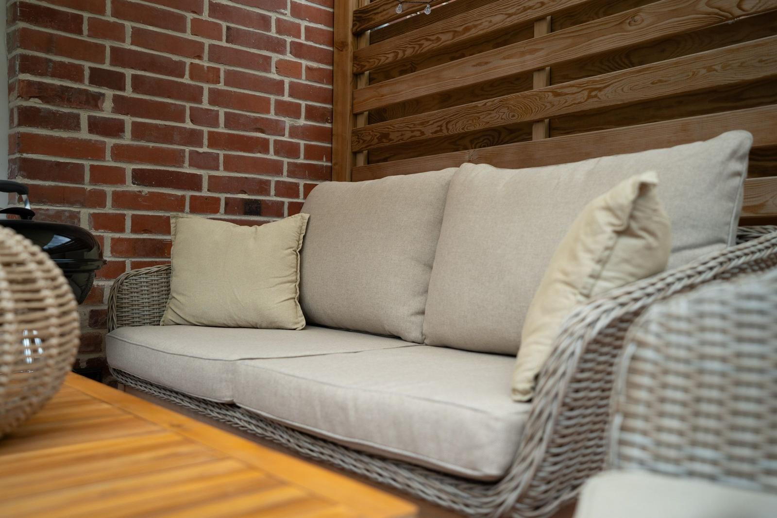 Wicker-Sofa mit Kissen an roter Ziegelwand und Holzgeländer.