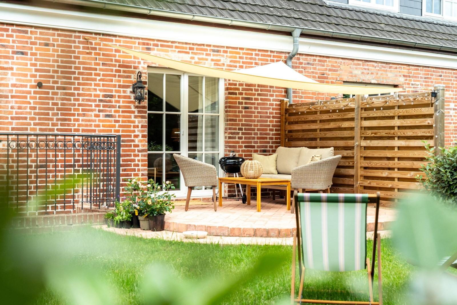 Terrasse mit Sitzgruppe, Grill und Sonnensegel vor Backsteinhaus.