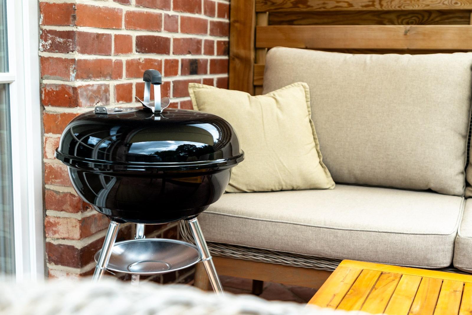 Schwarzer Grill auf Terrasse neben bequemer Sitzbank mit Kissen.