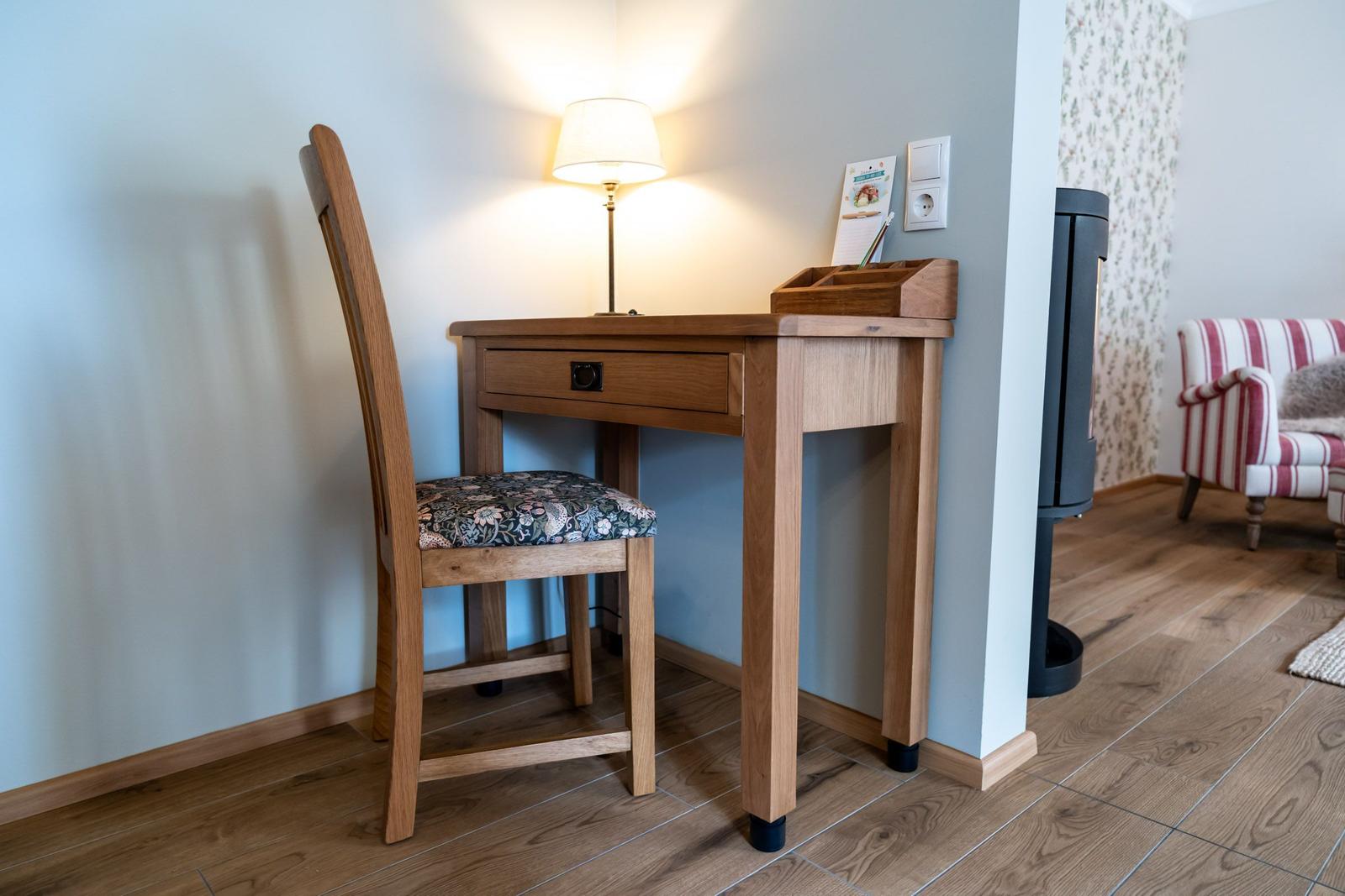 Schreibtisch mit Stuhl und Lampe an der Wand. Holzfußboden und Sessel im Hintergrund.
