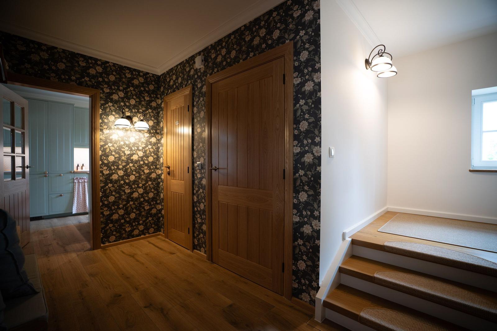 Flur mit Holzboden, floraler Tapete und Treppe zur oberen Etage.