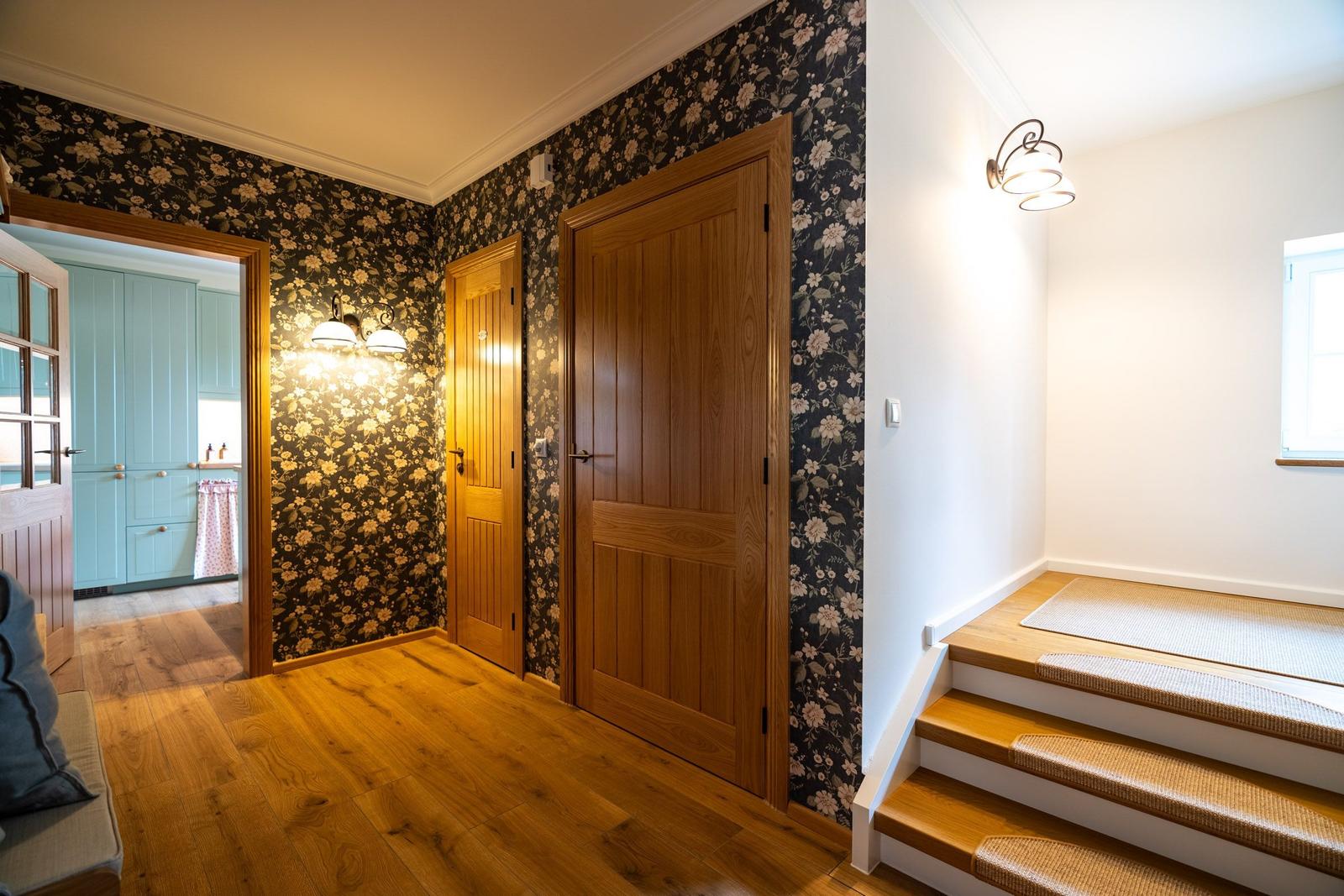 Hausflur mit Holzboden, floraler Tapete und Treppe zur oberen Etage.