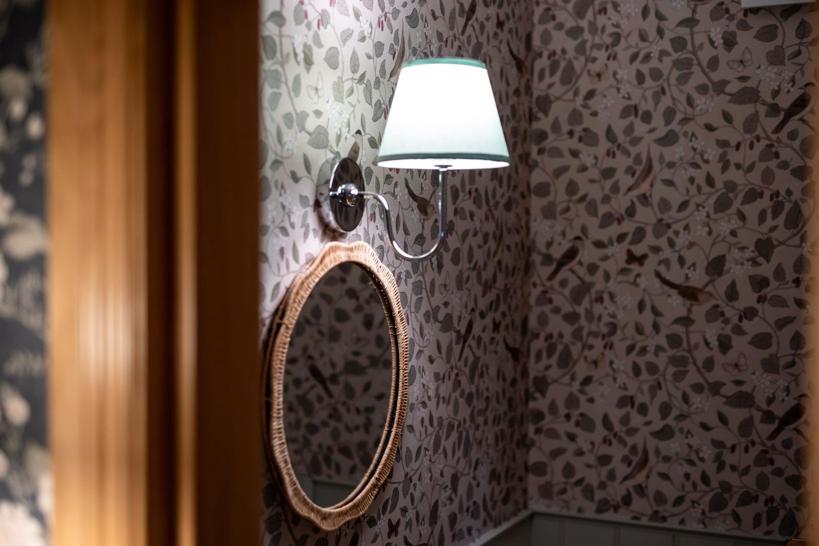 Wand mit floraler Tapete, runder Spiegel und Wandlampe mit Schirm