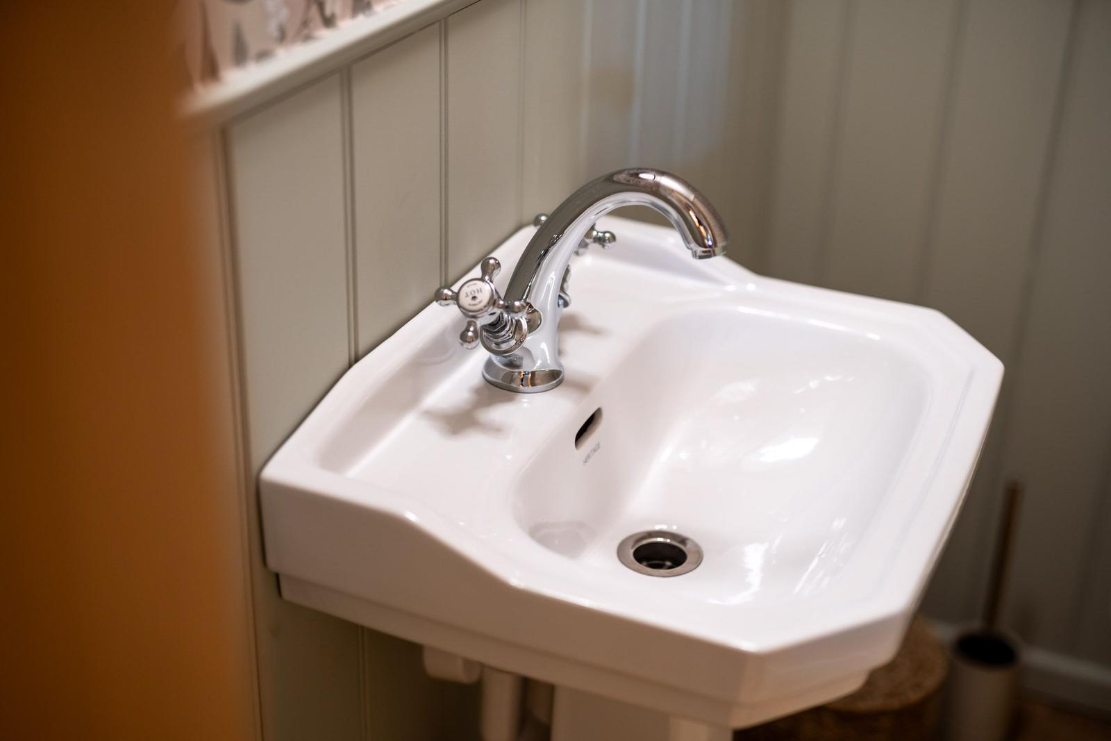 Weißes Waschbecken mit Chromarmatur an vertikal verkleideter Wand.
